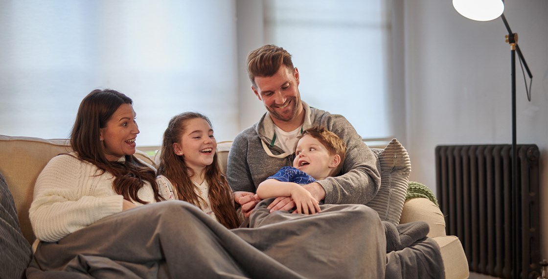 A family of four laughing and smiling while sitting on a couch